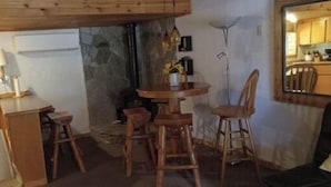 A compact kitchen with a microwave, stove, and sink. There is a dining area with a round table and wooden chairs. A stone wall and a floor lamp are also visible. - Reflections Inn (Kooskia)