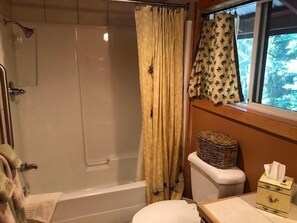 A bathroom with a bathtub, toilet, and a window with a view of trees.