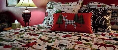 Een slaapkamer met een bed dat is overdekt met een quilt met dierenprinten, een rode lamp en kerstkussens.