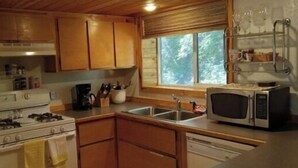 A compact kitchen with wooden cabinets, a gas stove, a microwave, and a sink. - Reflections Inn (Kooskia)