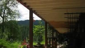 A covered outdoor area with a concrete floor, potted plants, and a wooden pergola structure. - Reflections Inn (Kooskia)
