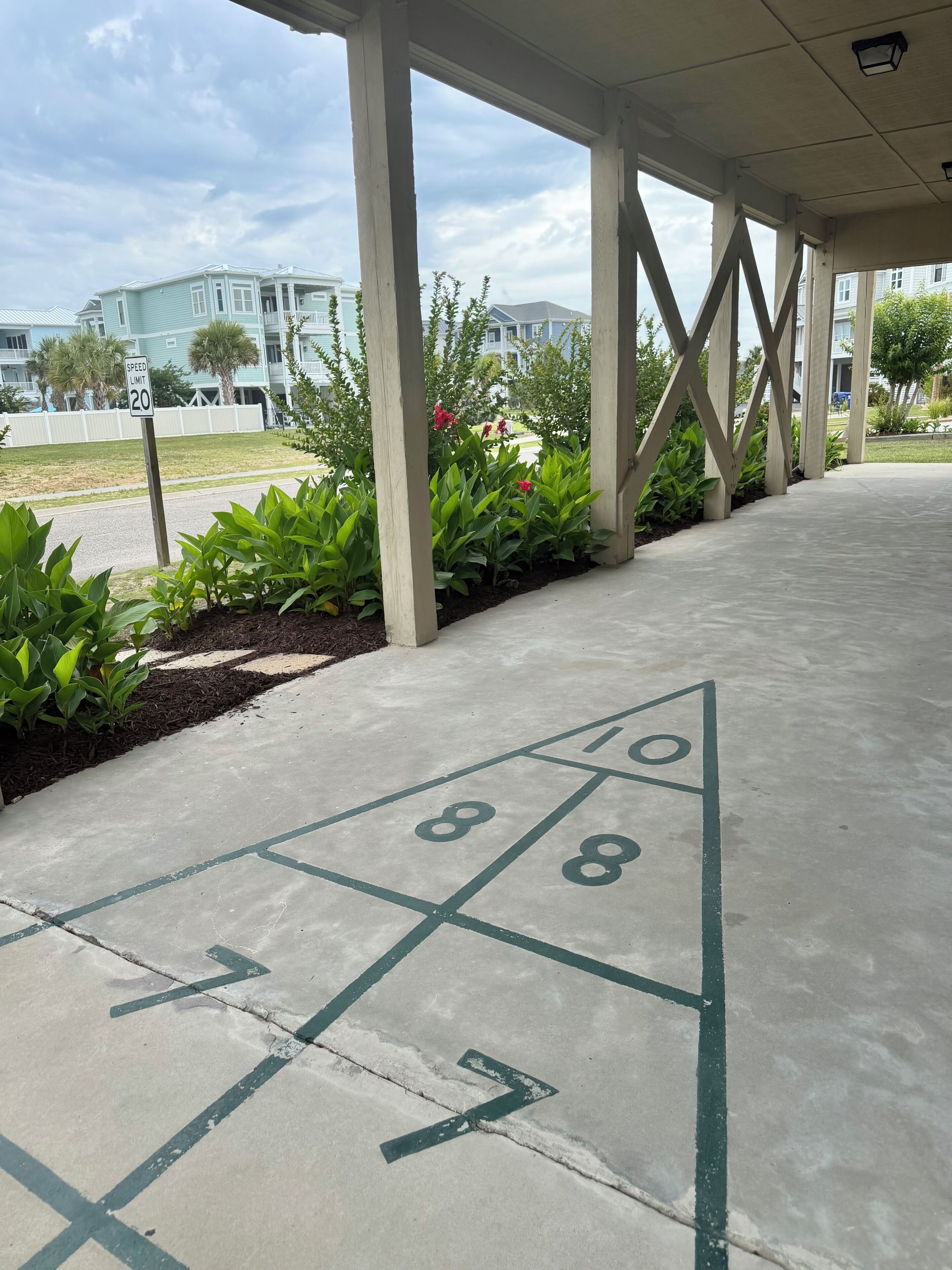 A shuffleboard court with a speed limit sign, surrounded by greenery and buildings.