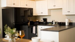 Une cuisine moderne avec des meubles blancs, un réfrigérateur noir et un coin café.