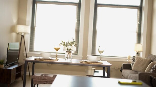 Un coin repas avec une table mise pour deux, un vase rempli de fleurs et une lampe.