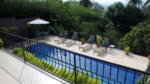 A poolside area with lounge chairs and a table, surrounded by greenery and a stone wall. - Playa Hermosa Ocean View Estate (Playa Hermosa)