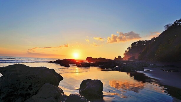 A sunset over a rocky coastline with calm waters reflecting the sky. - Playa Hermosa Ocean View Estate (Playa Hermosa)