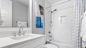Ein modernes Badezimmer mit einem weißen Waschbecken, Spiegel und einer Dusche mit weißen Fliesen.