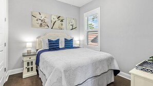 Ein Schlafzimmer mit Bett, Nachttischen, einem Fenster mit Jalousien und Wandbildern.