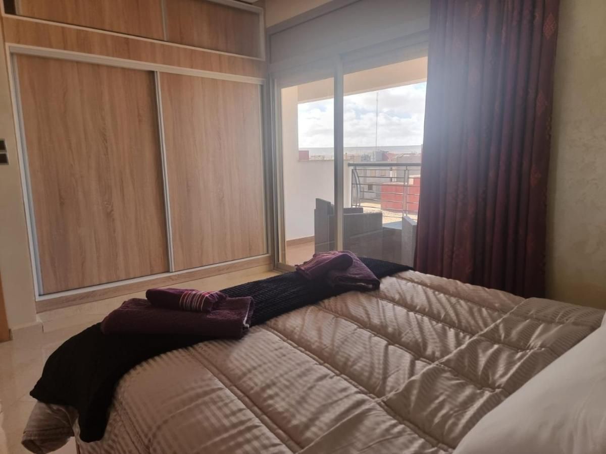 A hotel room with a large bed, a wooden wardrobe, and a view of the sky through a window.