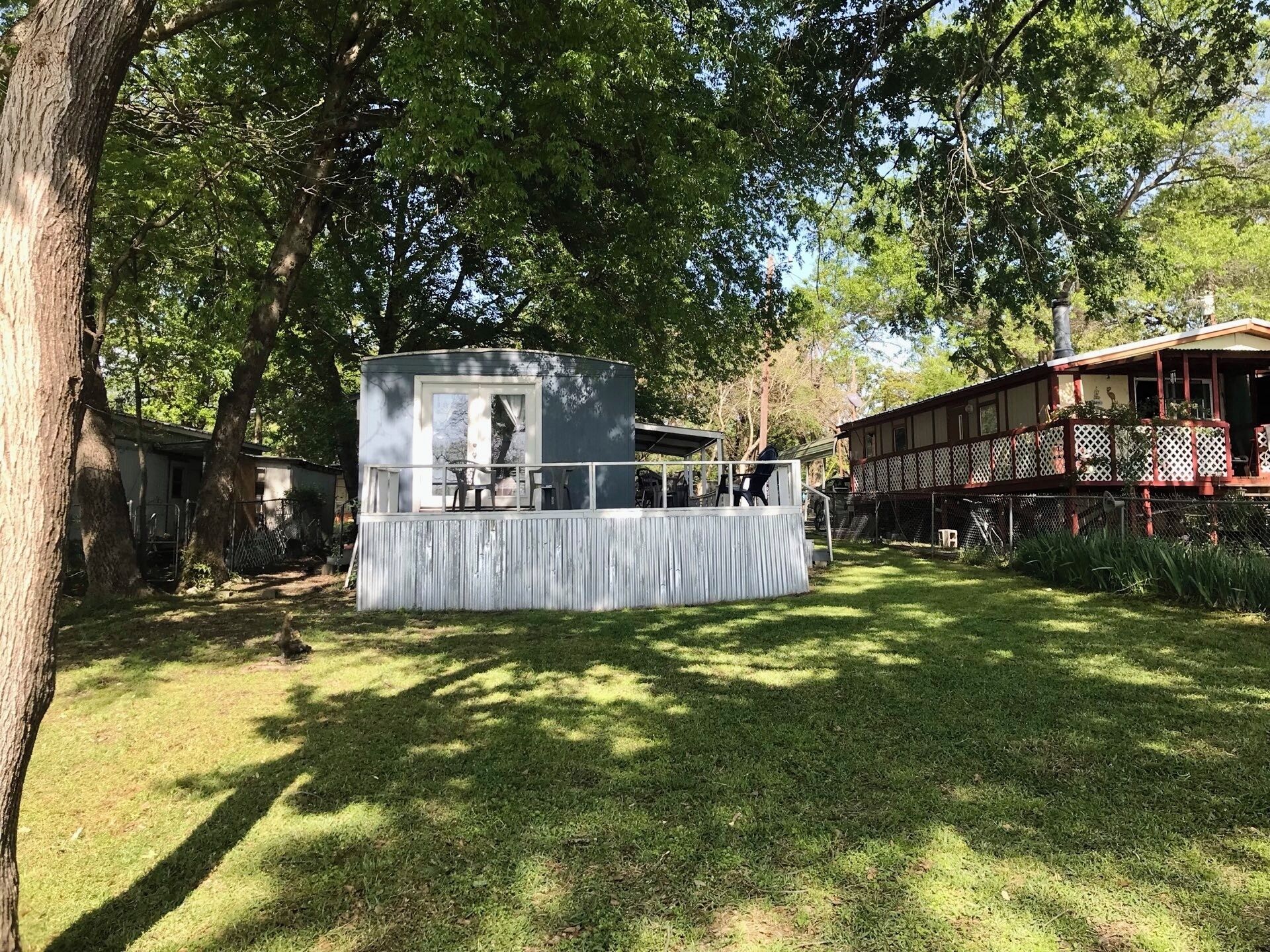 Une petite structure extérieure fermée, dotée d’un espace de repos abrité, entourée d’arbres et d’une pelouse.