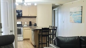Uma sala de estar moderna com um sofá de couro preto, uma poltrona cinza e um espaço de refeições com uma mesa pequena e cadeiras.
