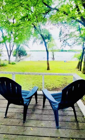 A wooden deck with two black chairs facing a grassy area and a body of water. - Waterfront Home Directly On Lake Tawakoni (Wills Point)