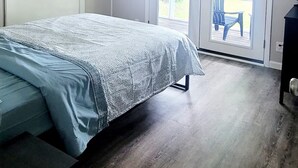 Quarto com cama, ventilador de teto e porta de vidro deslizante para área externa.