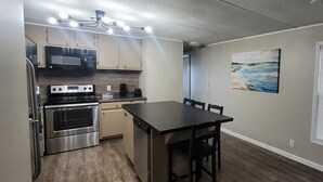 Cozinha compacta com micro-ondas, fogão e máquina de café. Há uma mesa de jantar com cadeiras e um quadro na parede.