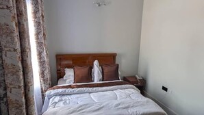 Een opgemaakt bed met een houten hoofdbord, een nachtkastje en een airconditioning aan de muur.