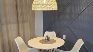 Zona pranzo con tavolo rotondo, quattro sedie, lampadario a sospensione e parete d'accento scura.
