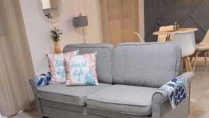 Un divano grigio con cuscini decorati, una poltrona blu, uno specchio rotondo e una lampada a sospensione in un soggiorno moderno.