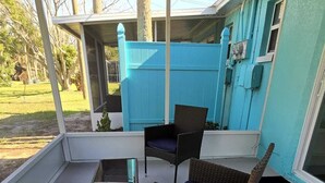 Un portico coperto con mobili in vimini, un tavolo in vetro e una recinzione blu sullo sfondo.