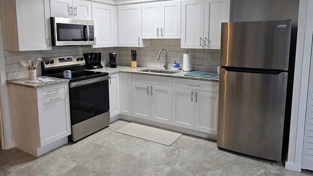 Una cucina moderna con mobili bianchi, un frigorifero in acciaio inossidabile, un forno a microonde, un forno e un lavello.