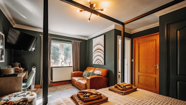 A bedroom with a four-poster bed, a leather armchair, a desk with a flat-screen TV, and a large window with curtains. - Boutique Shrewsbury Rooms (Shrewsbury)