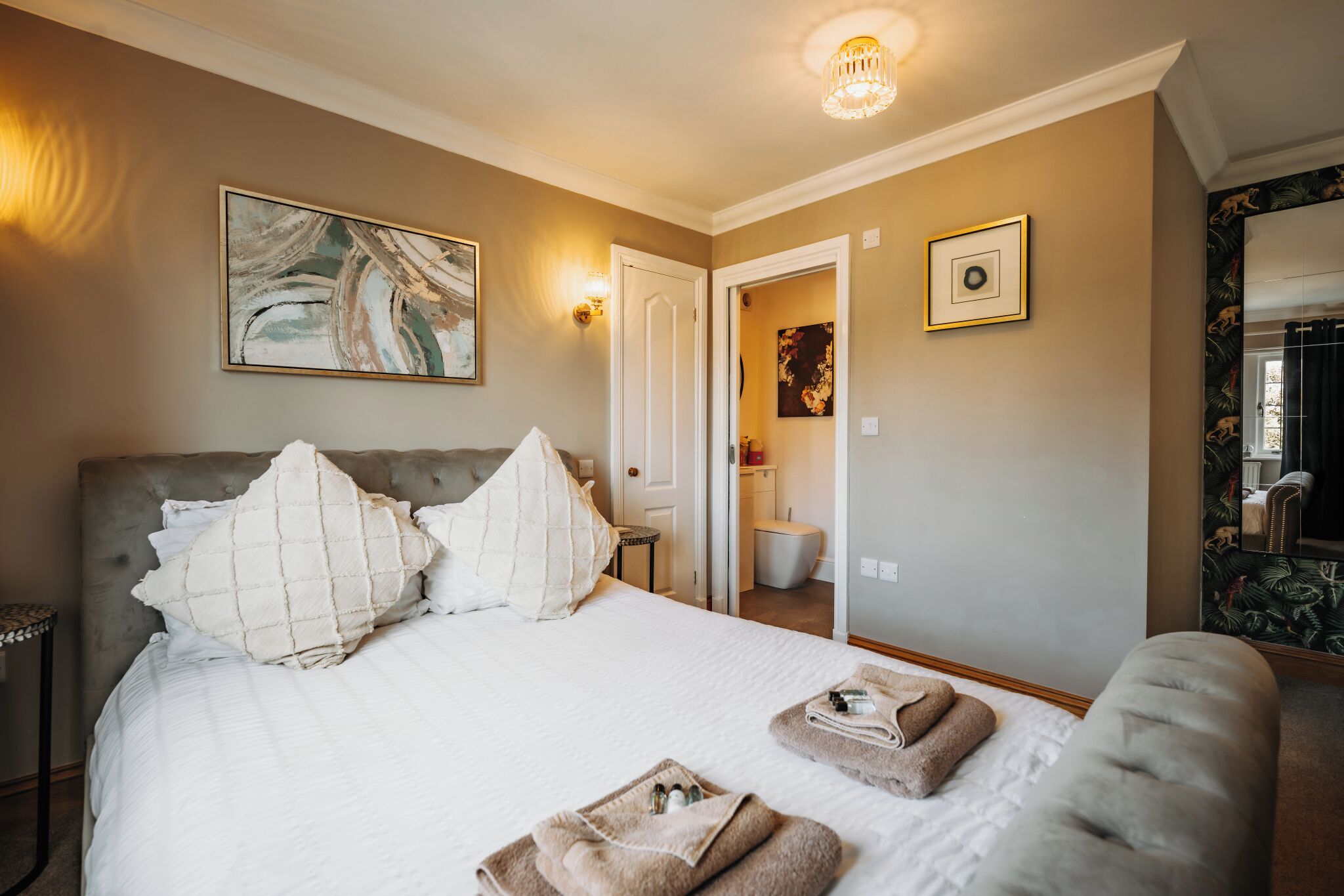 A hotel room with a large bed, a bedside table, a mirror, and a door leading to a bathroom.