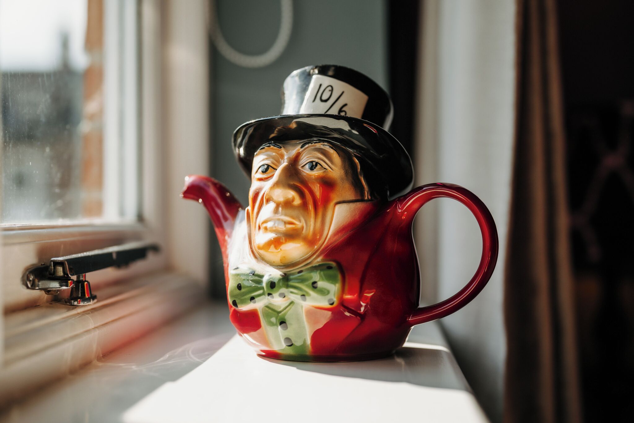 A ceramic teapot with a figure wearing a top hat on a windowsill.