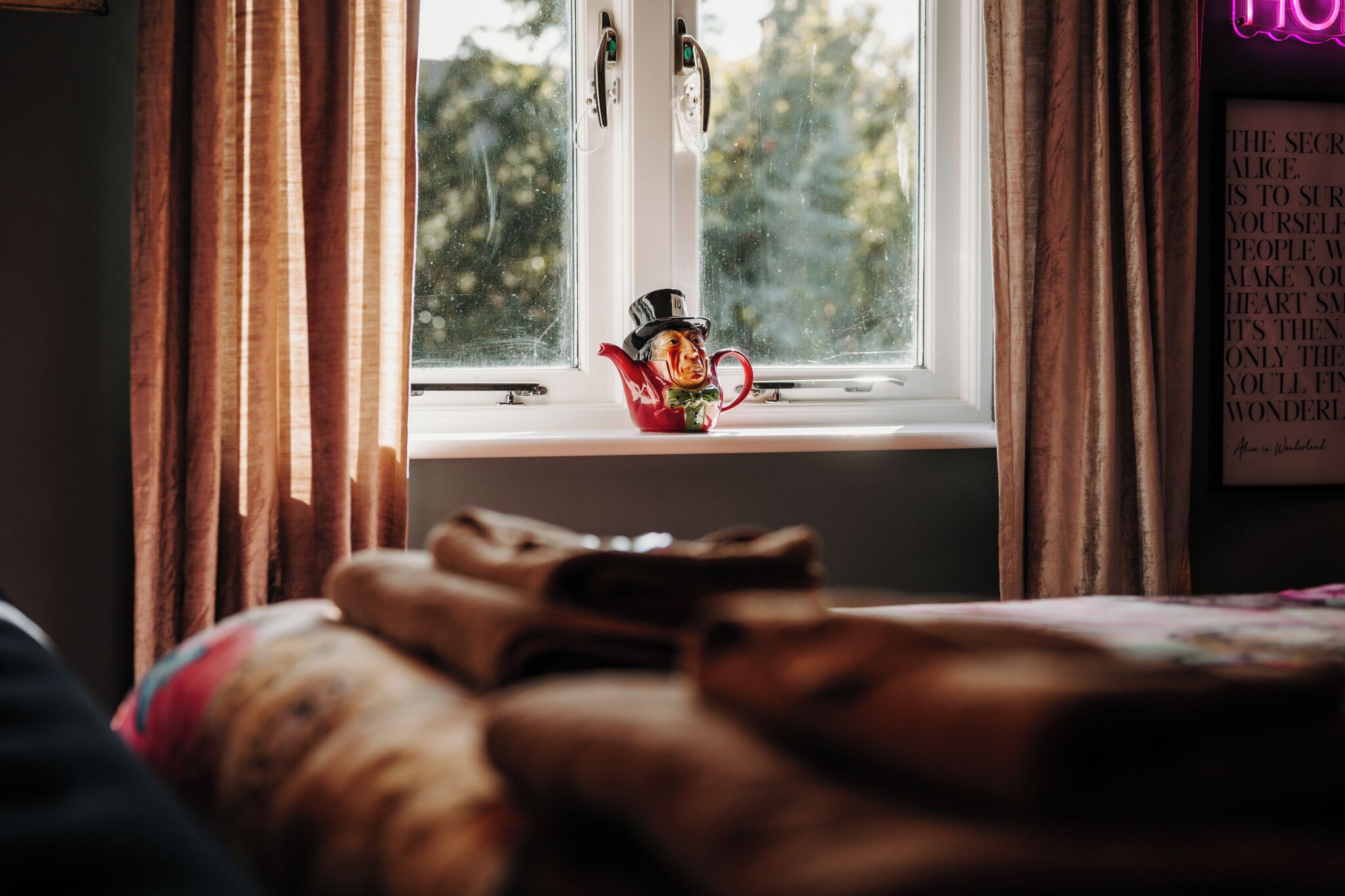 A room with a window, curtains, a bed, and a teapot on the windowsill.
