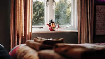 A room with a window, curtains, a bed, and a teapot on the windowsill.