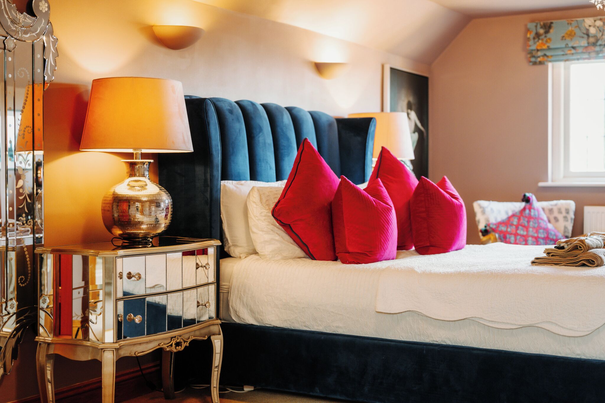 A bed with a white comforter, red pillows, and a blue headboard.