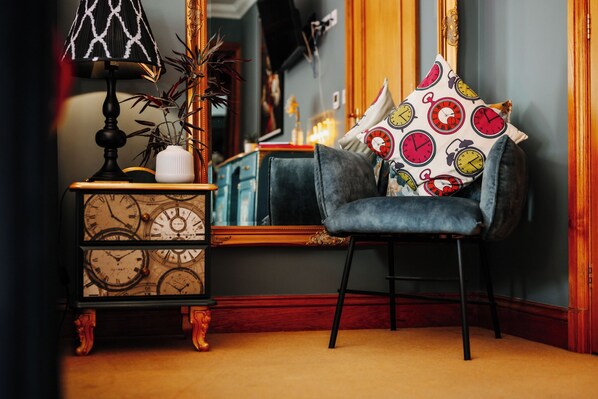 A cozy corner with a vintage clock, a lamp, and a chair with patterned cushions.