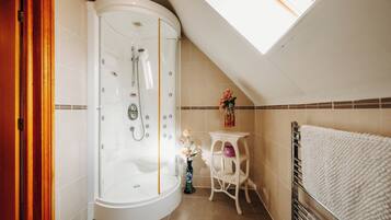 A modern bathroom with a walk-in shower, a small vanity with a vase of flowers, and a towel rack.