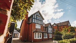 A Tudor-style house with a brick facade and white-framed windows, a paved driveway, and a metal fence. - Boutique Shrewsbury Rooms (Shrewsbury)
