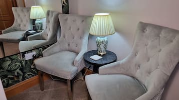 Una habitación con tres sillones tapizados, cada uno con una mesita auxiliar a juego y una lámpara. La habitación tiene una alfombra estampada y un espejo que refleja los muebles.