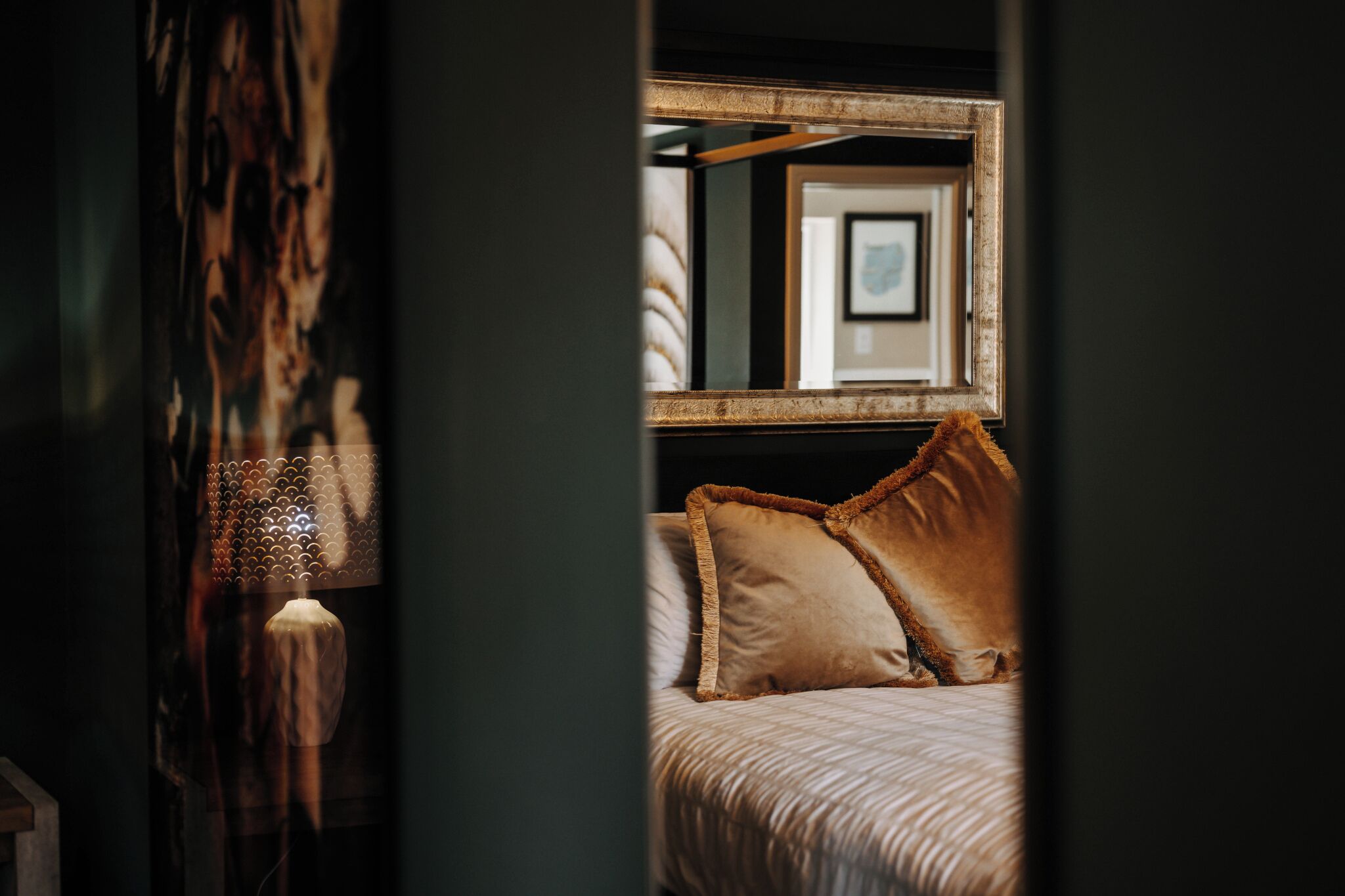 Une chambre à coucher avec un lit, des oreillers, un tableau encadré au mur et une lampe.