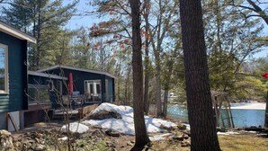A cabin with a deck, surrounded by trees and a lake.