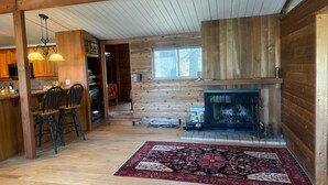 A spacious living area with a fireplace, wooden flooring, and a dining area with chairs.