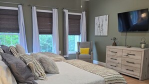 Une chambre avec un grand lit, un ventilateur de plafond, une télévision et une commode.