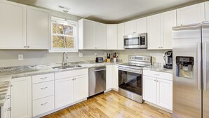 Una cocina moderna con gabinetes blancos, electrodomésticos de acero inoxidable, horno integrado y cafetera.