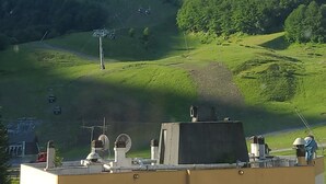 A mountainous landscape with a prominent peak, a green valley, and a building with antennas in the foreground.