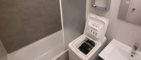 A modern bathroom with a bathtub, a built-in washing machine, and a sink.