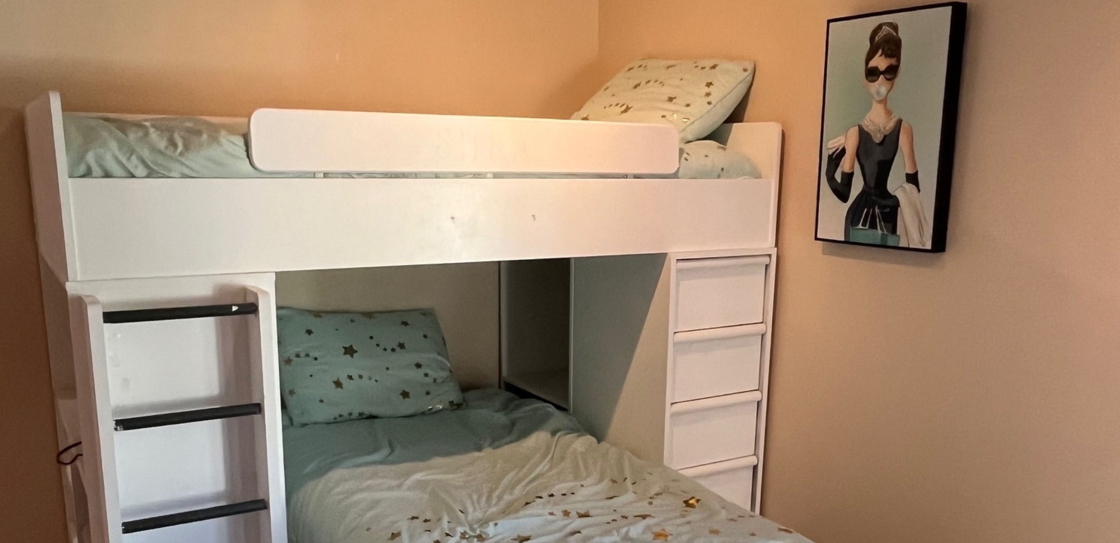 A bunk bed with a ladder, a lower bed with a pillow, and a dresser with drawers.