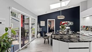 Una cocina moderna con una isla grande, un comedor con mesa y sillas, y vista al exterior a través de puertas de vidrio.