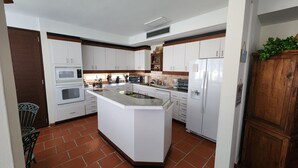 A kitchen with white cabinets, a central island, a refrigerator, and a microwave. - Villa Haven Giovanni (Vega Alta)