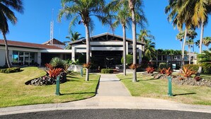 A modern hotel with a central entrance, palm trees, and a clear sky. - Villa Haven Giovanni (Vega Alta)