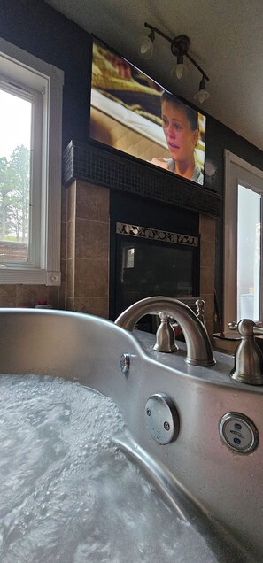 A bathroom with a bathtub, a sink with a faucet, and a television mounted above the sink.