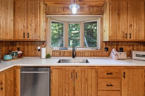 A kitchen with wooden cabinets, a stainless steel sink, a window with a view of trees, and a toaster. - Lake Superior Lakefront Cabin with its own Beach Access! (Herbster)