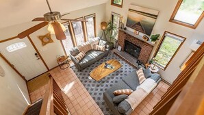 A spacious living room with a fireplace, a ceiling fan, and large windows.