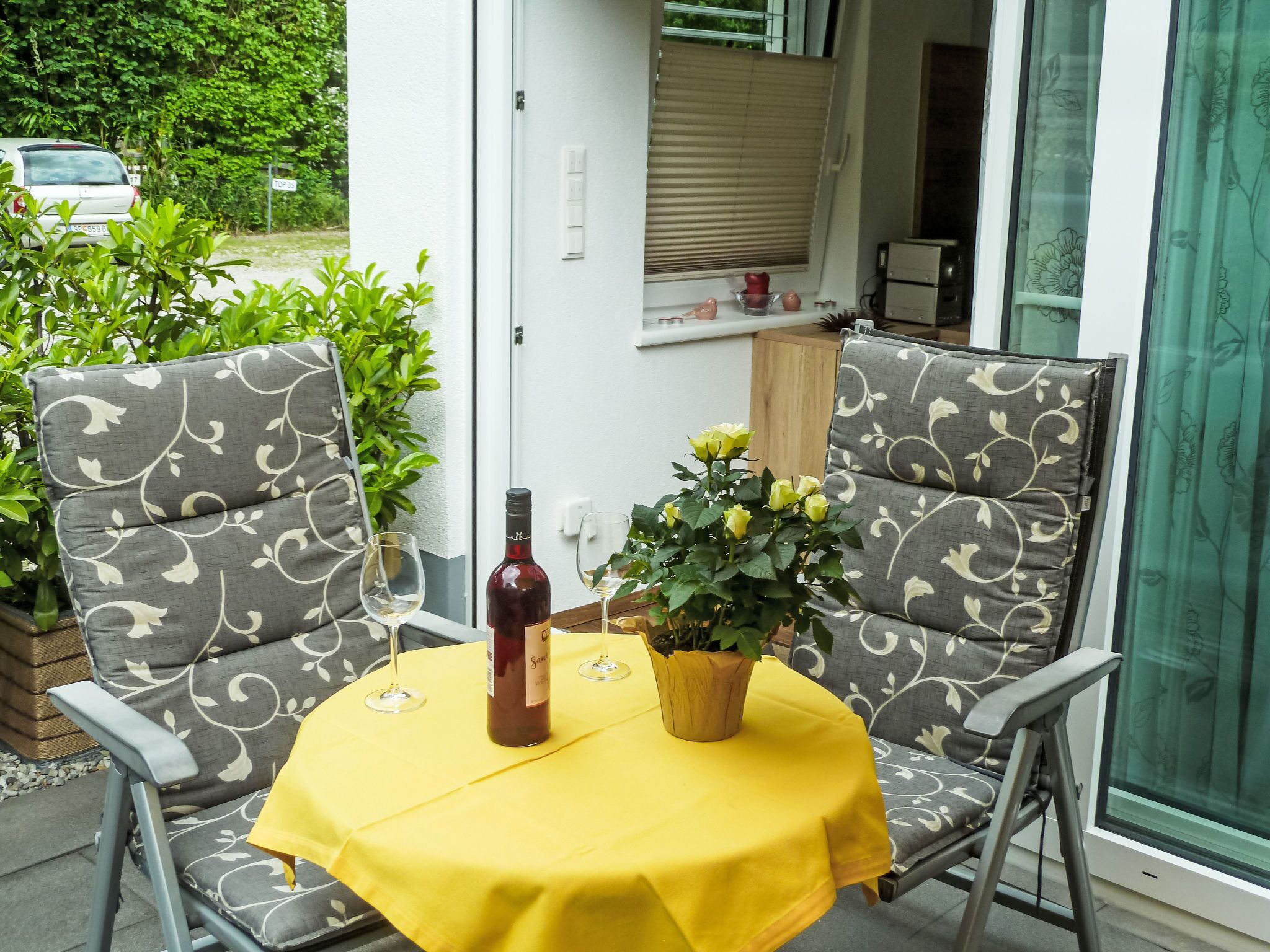A patio with two grey upholstered chairs, a yellow tablecloth, a bottle of wine, and a potted plant.
