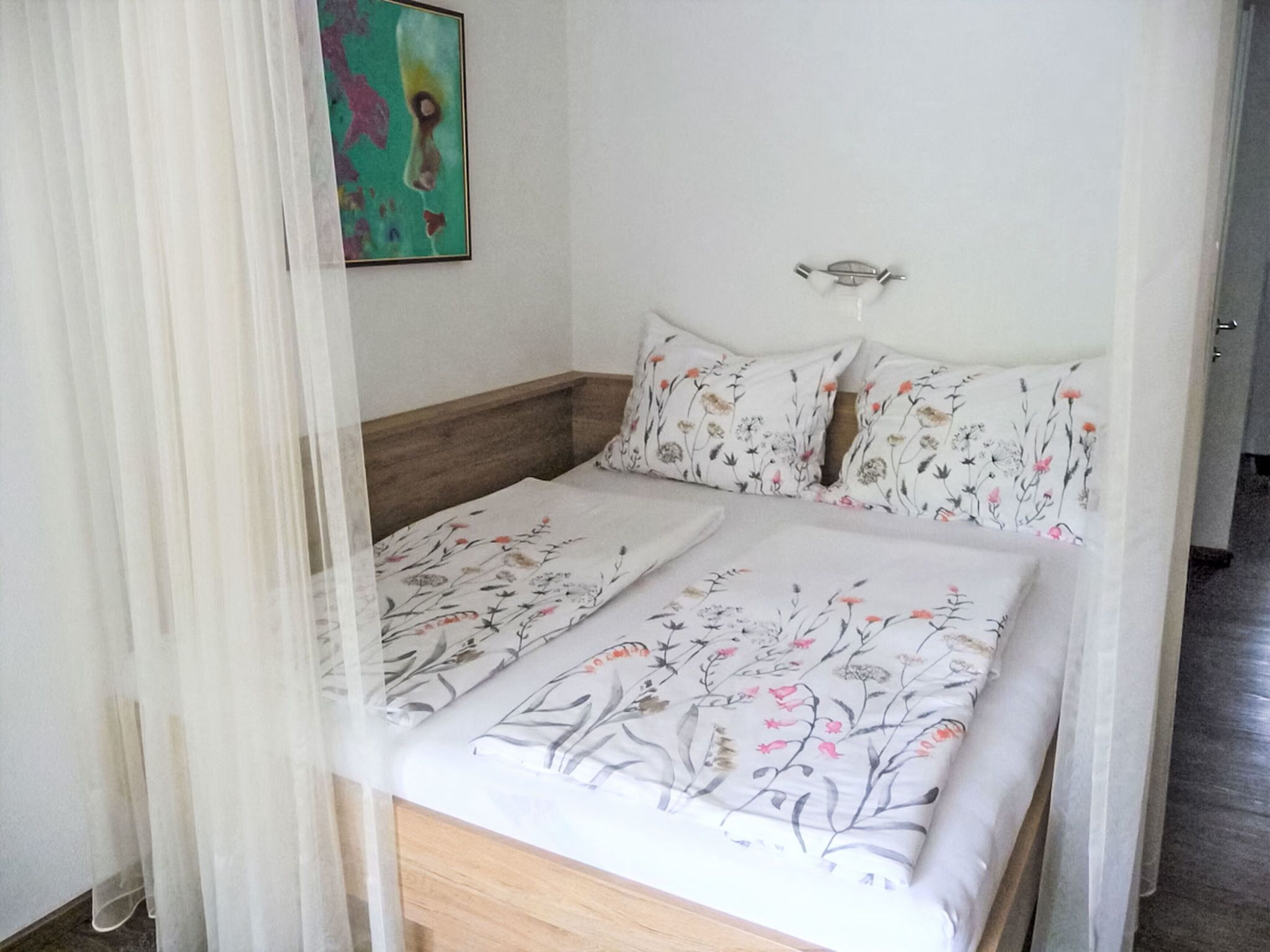 Un lit avec une literie à motifs floraux, une tête de lit en bois et un luminaire fixé au mur.
