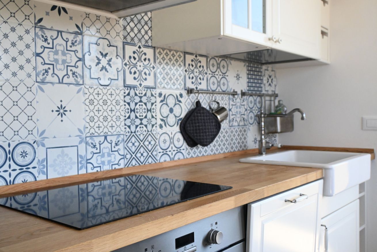 A kitchen with patterned tiles, a wooden countertop, a sink, and a stove.